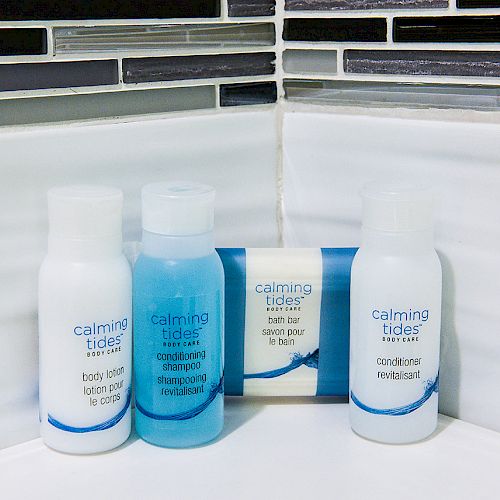 The image shows three 'Calming Tides' brand toiletries (lotion, shampoo, conditioner) and a bar of soap, set against white and grey bathroom tiles.