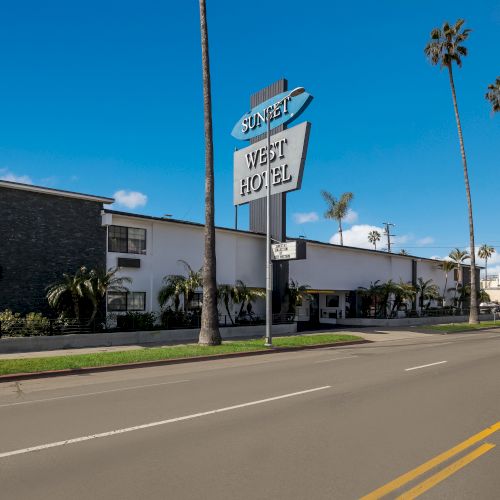 Image of a retro-style hotel with a large sign reading "Sunset West Hotel," palm trees lining the street, and clear blue skies.