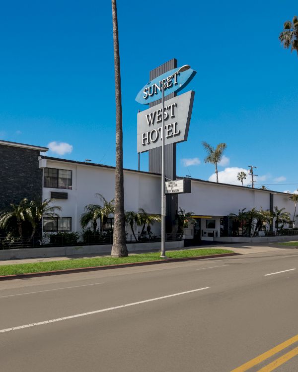 Image of a retro-style hotel with a large sign reading "Sunset West Hotel," palm trees lining the street, and clear blue skies.