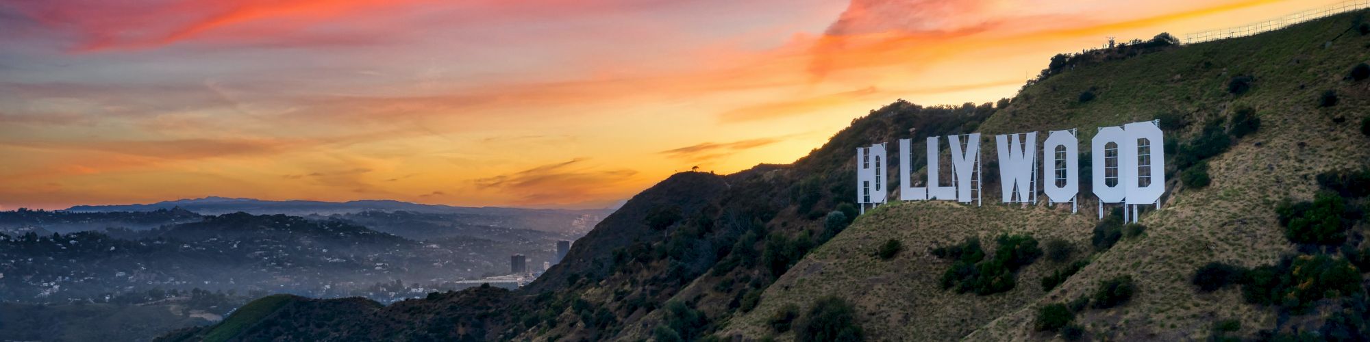 The image depicts the iconic Hollywood sign on a hillside at sunset, with a colorful sky and distant landscape in the background, ending the sentence.