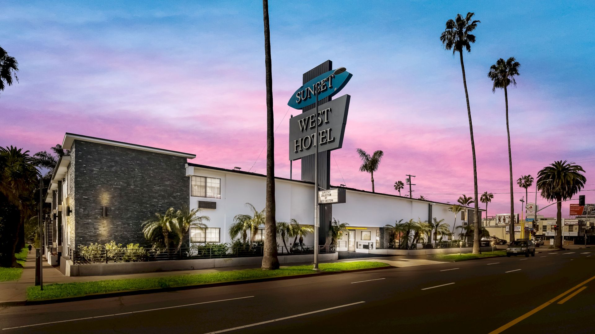 A modern motel with a "Sunset West Hotel" sign, palm trees, and a pink and blue sky in the background.