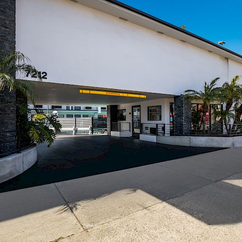 This image shows the entrance to a modern building with the number 7212, featuring palm trees and a clean, wide path leading to the entranceway.