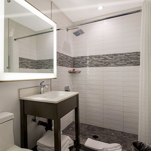 This image shows a modern bathroom with a shower, sink, toilet, and mirror. The design is sleek with white tiles and a gray accent.