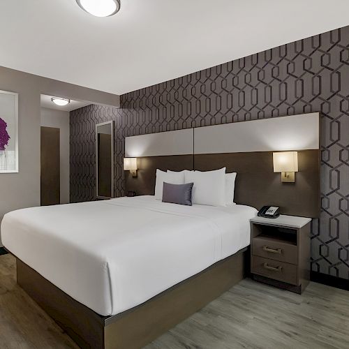 A modern hotel room with a large bed, decorative wallpaper, two nightstands with lamps, framed wall art, and a phone on one nightstand.