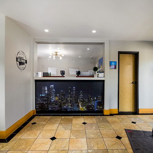 The image shows a modern reception area with two doors, a counter with a cityscape design, a logo on the wall, tile flooring, and some chairs.