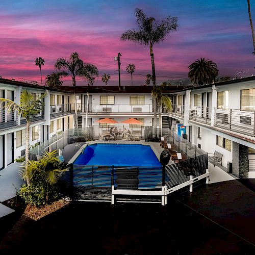 The image shows a courtyard of a two-story motel or apartment complex with a swimming pool in the center, surrounded by balconies and palm trees.