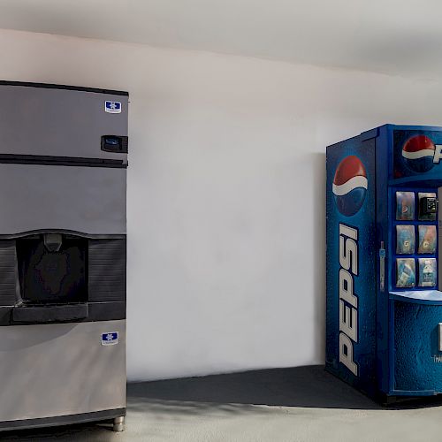 The image shows a Pepsi vending machine next to an ice dispenser against a white wall.