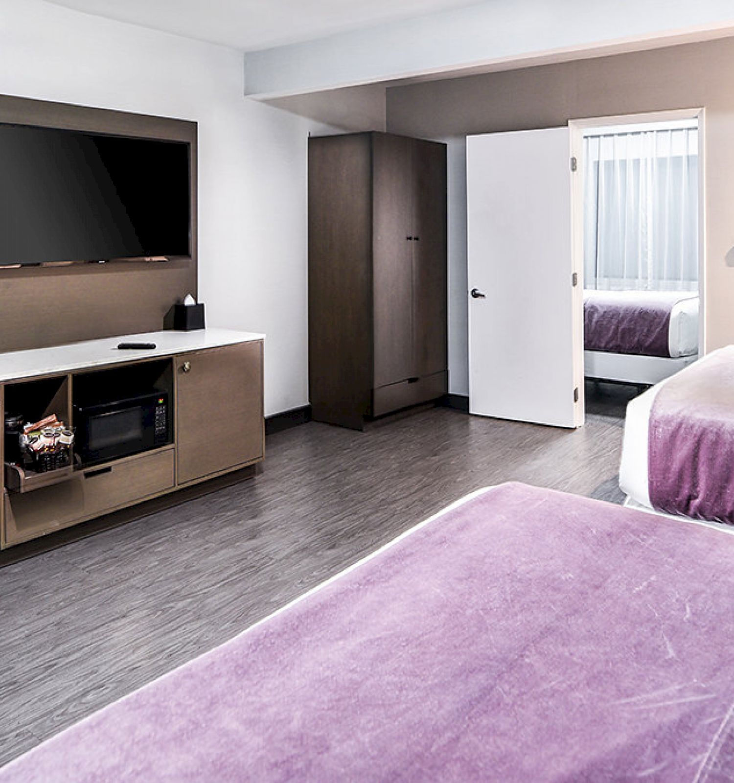 The image shows a hotel room with two beds, a TV, a desk with a chair, and a microwave. There is a closet and a door leading to the bathroom.